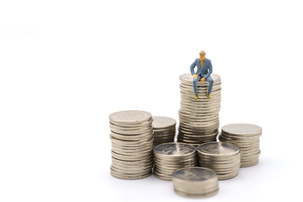 Entreprise, investissement monétaire et concept d'équipe. La figure miniature d'homme d'affaires figure assise sur une pile de pièces d'argent sur fond blanc.