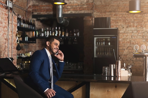 Entreprise joyeuse parlant au téléphone, assise au comptoir du bar, ayant une conversation réussie et agréable, espace de copie