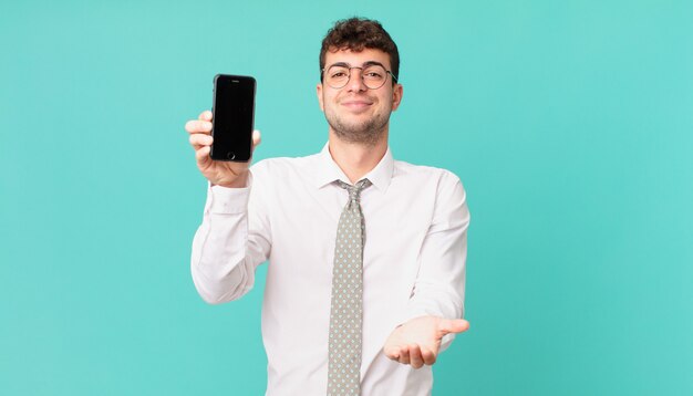 Entreprise avec un smartphone souriant joyeusement avec un regard amical, confiant et positif, offrant et montrant un objet ou un concept