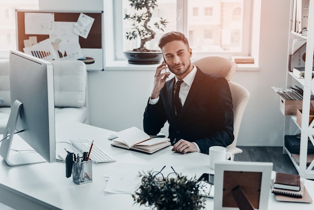 Entretien d'affaires agréable. Beau jeune homme en costume complet parlant au téléphone et regardant loin