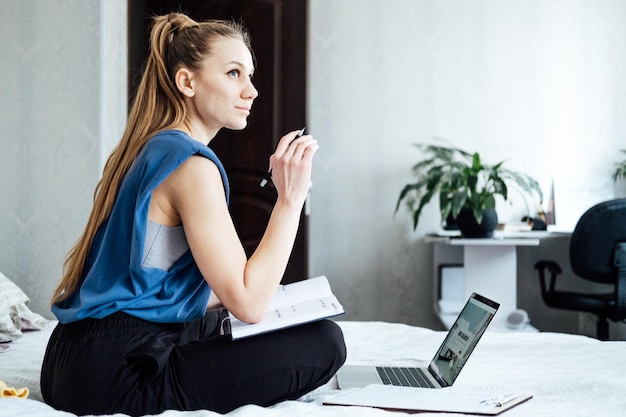 Entretien d'embauche Trouver un nouvel emploi Jeune femme écrivant dans le journal du planificateur notes sur l'entretien d'embauche assis près d'un ordinateur portable sur le lit à la maison