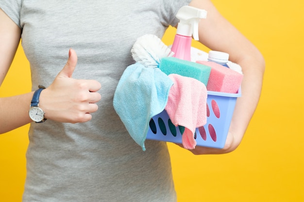 Entretien ménager de qualité. Femme au foyer pouce vers le haut. Femme avec panier de produits de nettoyage sur jaune.