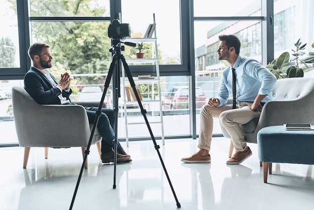 Photo entretien de tournage. deux jeunes hommes en tenue décontractée et élégante parlent tout en faisant une nouvelle vidéo à l'intérieur