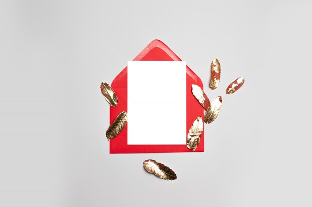 Enveloppe d'affaires rouge avec du papier blanc et des feuilles d'or sur fond gris.