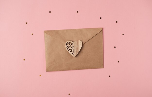 Enveloppe artisanale avec coeur en bois dessus sur fond rose avec des étoiles. Lettre d'amour romantique pour le concept de la Saint-Valentin. Vue de dessus.