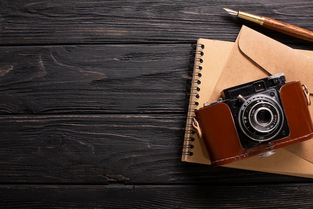 Une enveloppe un bel appareil photo et un cahier avec un stylo sur un fond en bois noir avec une place pour une inscription