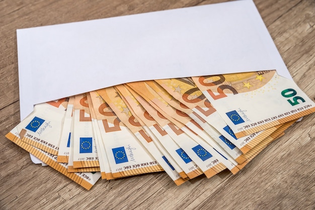 Photo enveloppe blanche avec des billets en euros sur bois