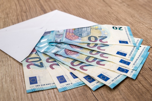 Enveloppe blanche avec des billets en euros sur fond de bois