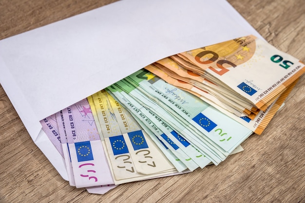 Enveloppe blanche avec des billets en euros sur une surface en bois