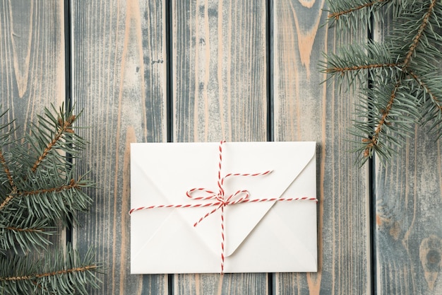 Enveloppe blanche sur fond de bois gris avec des branches d'arbre de Noël attachées avec un cordon avec un arc Vue de dessus