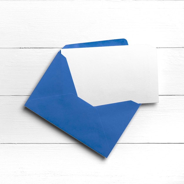 Enveloppe bleue avec carte postale ou carte de voeux sur table en bois blanc