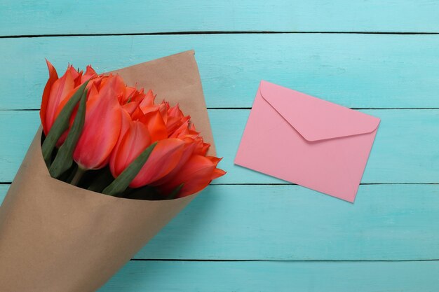 Enveloppe et bouquet de tulipes rouges sur fond de bois bleu. Anniversaire, Saint Valentin ou demande en mariage. Vue de dessus