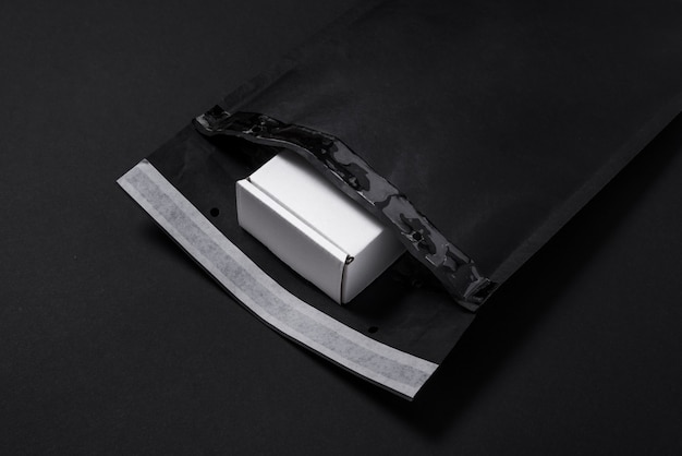 Enveloppe à bulles de papier noir et boîte en carton blanc sur fond sombre