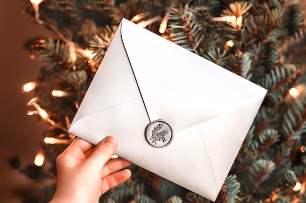 Enveloppe cadeau de Noël dans une main d'enfant parmi les branches d'arbres de Noël