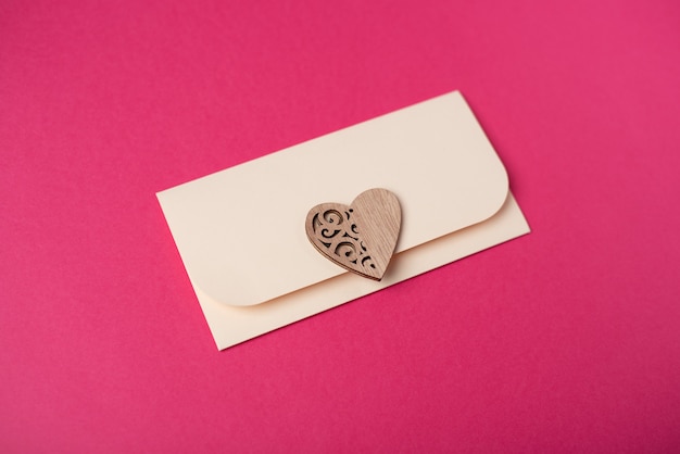 Photo une enveloppe avec le coeur en bois sur le fond rose chaud. concept de la saint-valentin.