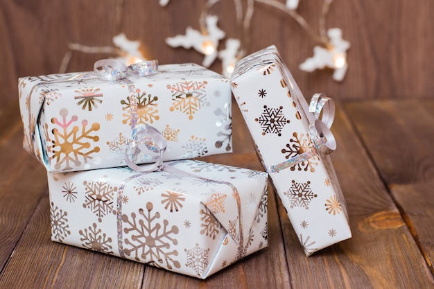 Photo enveloppé dans des boîtes-cadeaux d'emballage festives attachées avec un ruban d'argent et une guirlande de cerfs de noël sur une table en bois. préparer pour noël