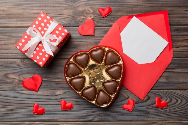 Enveloppe sur fond coloré pour la Saint-Valentin avec boîte-cadeau et chocolat en forme de coeur avec boîte-cadeau de chocolats vue de dessus avec espace de copie