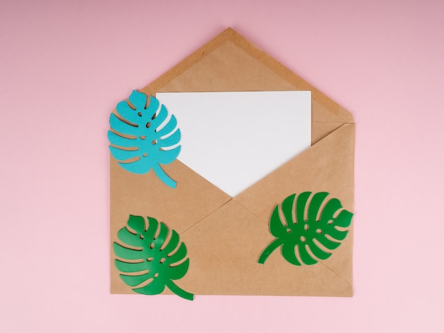 Une enveloppe kraft et un morceau de papier blanc, avec des feuilles de papier monstera en haut.