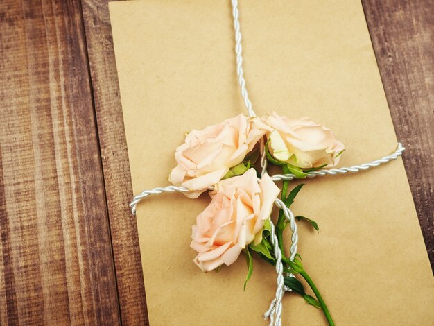 Enveloppe kraft, vieux papier noué avec une corde, vieille ficelle, au-dessus de roses doucement roses, le concept d'un cadeau.