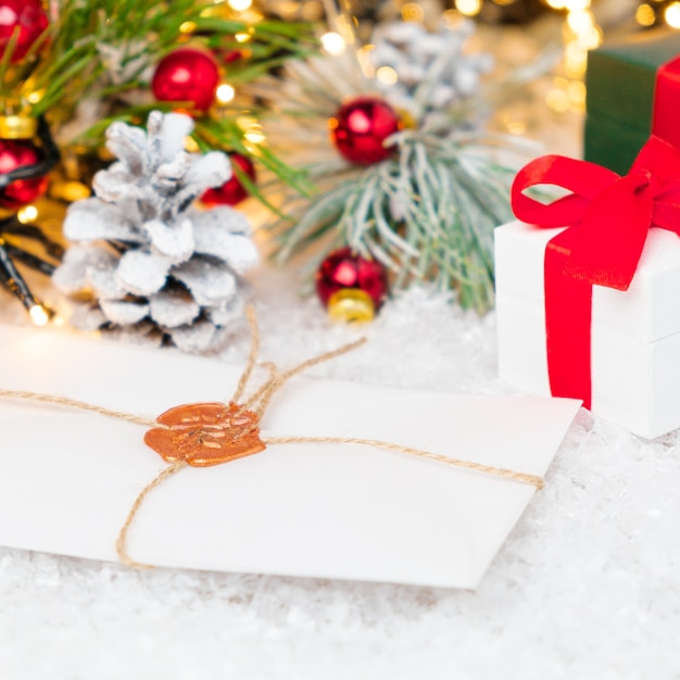 Une enveloppe avec une lettre au Père Noël, des coffrets cadeaux sous un arbre de Noël décoré sur la neige.