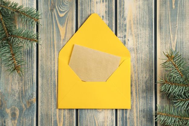 Enveloppe de Noël ouverte jaune sur fond de bois gris avec carte de voeux en papier kraft vierge Espace de copie Vue de dessus