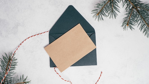 Enveloppe de Noël ouverte verte sur fond de béton blanc avec carte de voeux en papier kraft vierge. Espace de copie. Vue de dessus