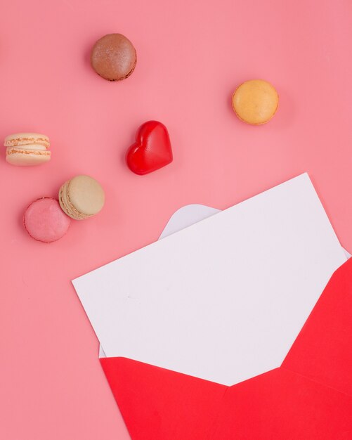 Enveloppe ouverte avec vide vide, coeur et macarons sur fond rose