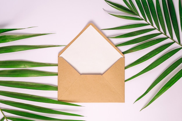 Enveloppe en papier brun kraft avec carte vide blanche sur les feuilles de palmier, fond blanc, maquette lettre vierge