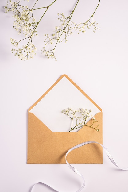 Enveloppe en papier brun kraft avec carte vide blanche, fleurs de gypsophile et ruban de tissu, fond blanc, maquette lettre vierge