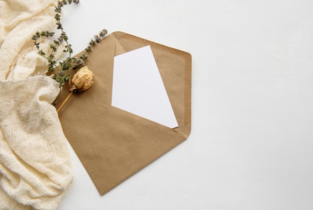 Une enveloppe en papier kraft une carte vierge blanche et des fleurs séchées sur une table blanche Vue de dessus de fond de vacances à la mode