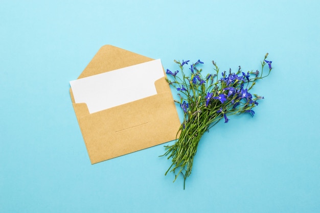 Photo une enveloppe postale ouverte avec une feuille de papier et un bouquet de fleurs sauvages sur fond bleu. le concept de correspondance amoureuse. mise à plat.