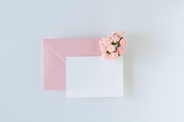 Enveloppe rose avec carte et roses sur fond blanc