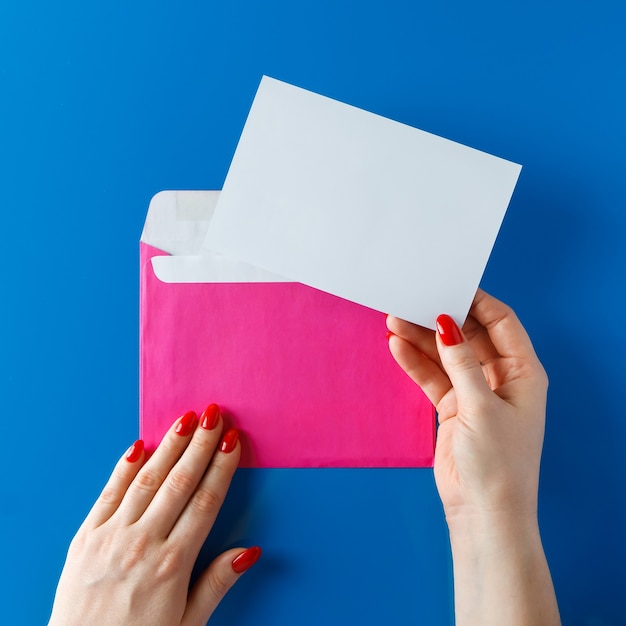 Enveloppe rose avec une carte vierge en mains sur bleu