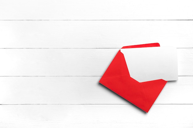 Enveloppe rouge avec carte postale ou carte de voeux sur table en bois blanc