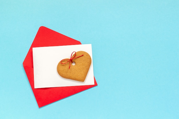 Enveloppe rouge et carte vierge de texte et de biscuits au gingembre en forme de coeur sur fond bleu.
