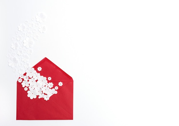Enveloppe rouge avec des fleurs en papier blanc sur fond blanc avec espace de copie