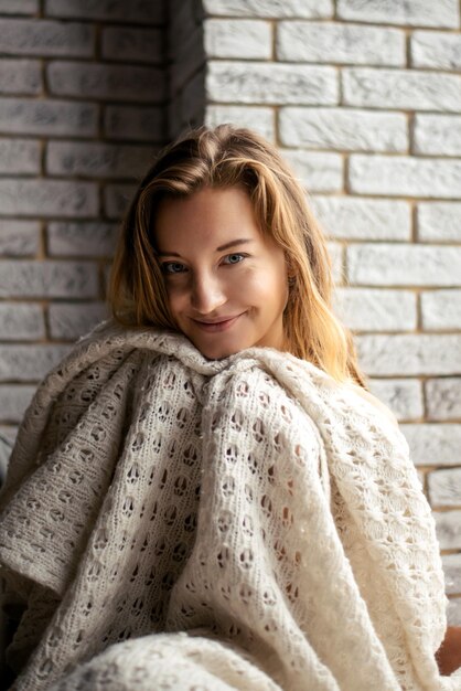 Enveloppée dans une confortable couverture blanche, une jeune femme sourit doucement à la caméra. L'image incarne l'essence du confort et de la sérénité, évoquant un sentiment de calme.