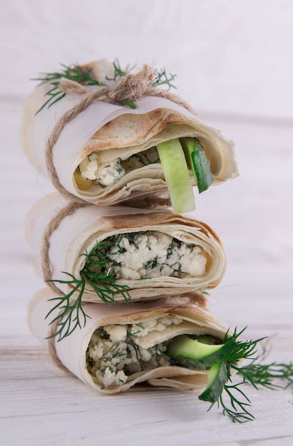 Enveloppements de tortilla avec du fromage cottage, de l'aneth et du concombre sur fond de bois.