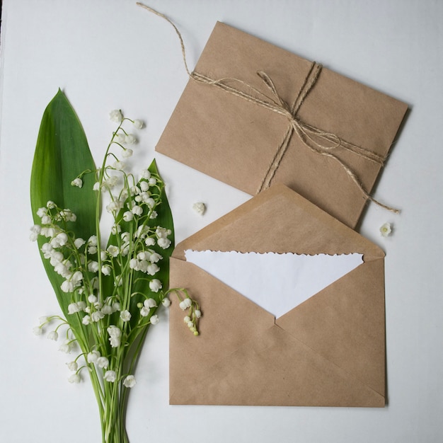 Enveloppes artisanales beiges, carte vierge blanche et bouquet de Lys de la vallée.