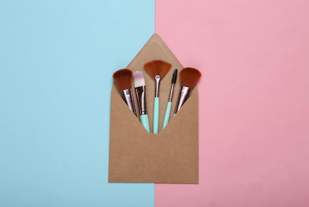 Enveloppes artisanales avec pinceaux de maquillage sur fond bleu rose Vue de dessus