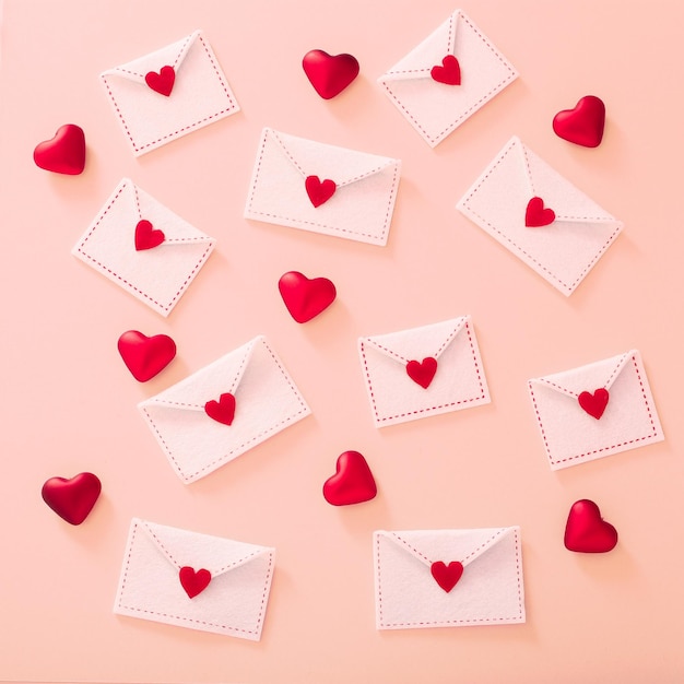 Photo enveloppes en feutre blanc avec des coeurs rouges sur la vue de dessus de fond rose clair