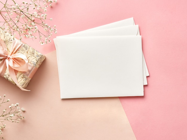 enveloppes vierges sur fond rose ou beige avec fleurs et cadeau. Vue depuis le sommet.