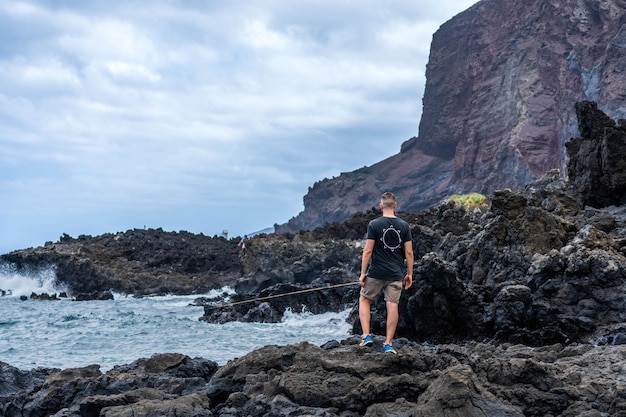 L'envers du jeune homme caucasien debout dans les rochers noirs près de la mer