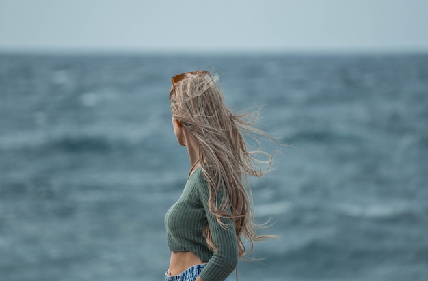 L'envers d'une femme aux cheveux blonds regardant l'infini près de la mer