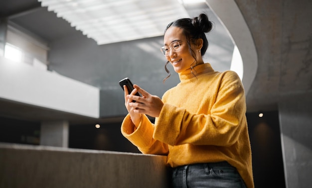 Envoyer des SMS au téléphone et une femme dans un immeuble de bureaux heureuse et souriante lors de la recherche et de la lecture sur Internet Fille asiatique et entrepreneur d'affaires sur smartphone pour rechercher des médias sociaux ou naviguer au Japon