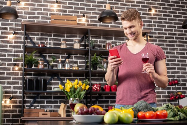 Envoyer Un Texto à Sa Femme. Bel Homme Aux Cheveux Blonds Portant Un Jean Et Un T-shirt Buvant Du Vin Et Envoyant Des Sms à Sa Femme