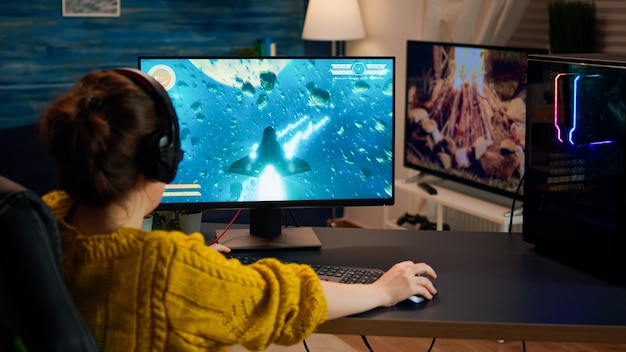 Sur l'épaule femme gamer jouant à un jeu de tir professionnel en ligne sur ordinateur à la maison tard dans la nuit. Joueur professionnel testant des jeux vidéo en ligne sur PC avec un réseau de technologie moderne sans fil.