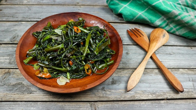 Photo Épinards d'eau sautés ou tumis kangkung nourriture indonésienne servie sur une assiette en bois sur une table en bois