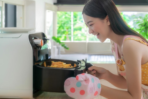 Photo Épouse asiatique cuisinant des frites sans huile en utilisant sa friteuse électrique dans sa cuisine à la maison