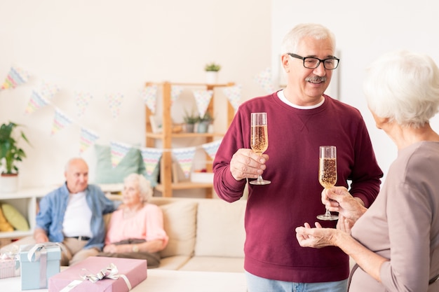 Les époux âgés de grillage avec des flûtes de champagne tout en célébrant des vacances avec des amis